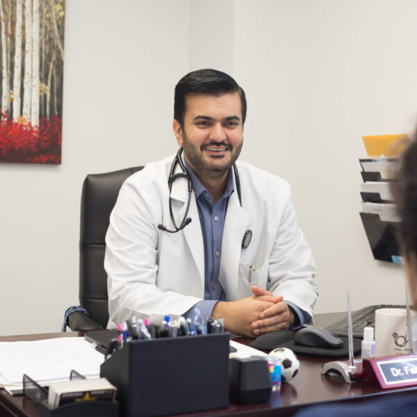 A medical doctor sitting at a desk talking with a patient.